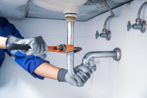 technician plumber using a wrench to repair a water pipe under t